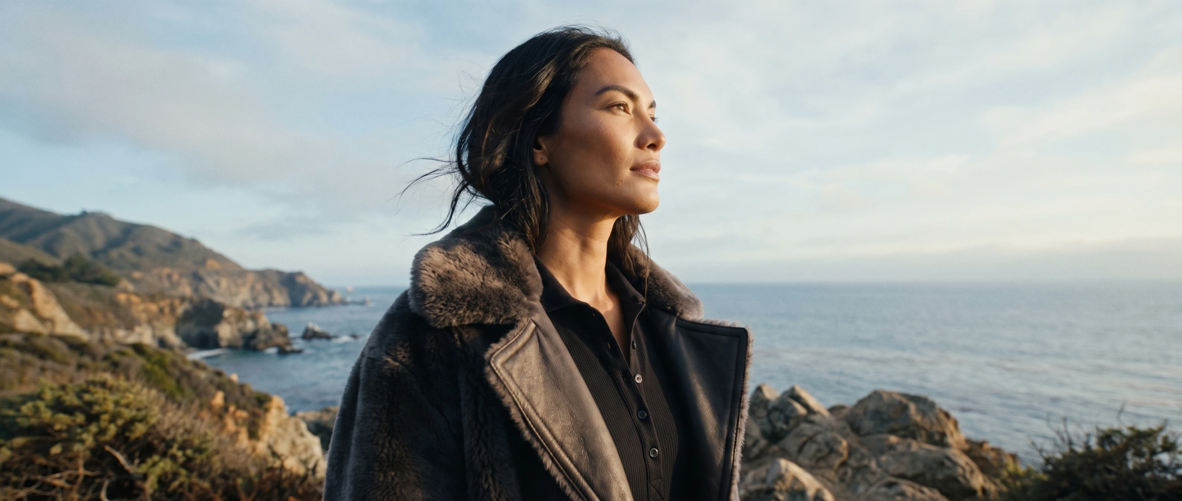 Woman standing on a coastal cliff at dusk.